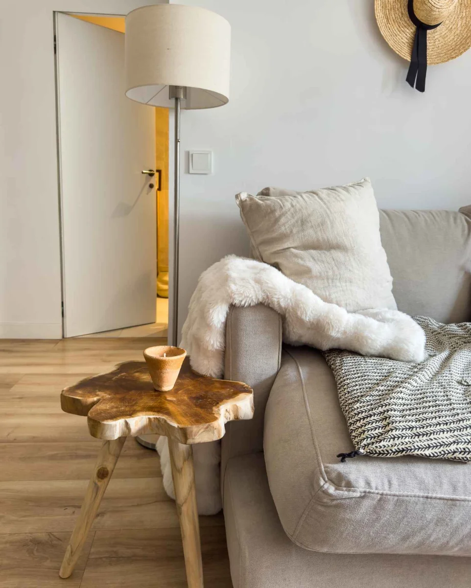 Taburete de madera de teca Tramontana como mesa auxiliar junto a sofá en salón moderno
